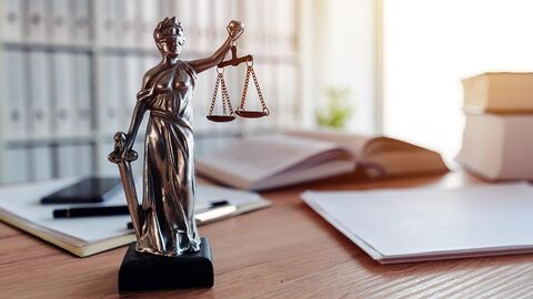 Justitia-Statue auf einem Schreibtisch vor einer Bücherwand