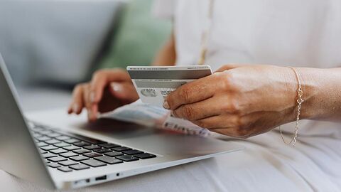 Frau arbeitet am Notebook und hält eine Bankkarte in einer Hand.