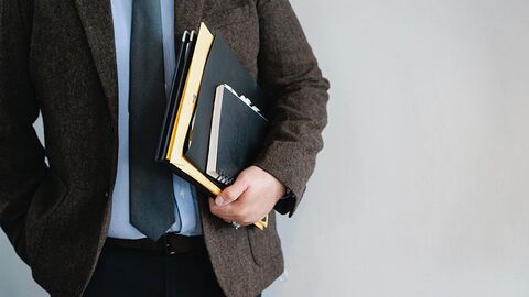 Mann im Anzug trägt Akten unter einem Arm.