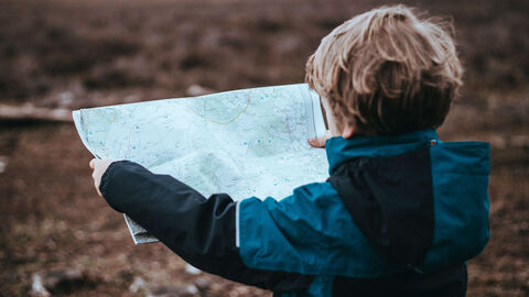 Junge steht auf einem Feld und schaut auf eine aufgeklappte Landkarte.