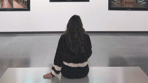 Frau sitzt auf dem Boden eines Raums und betrachtet Bilder an der Wand.